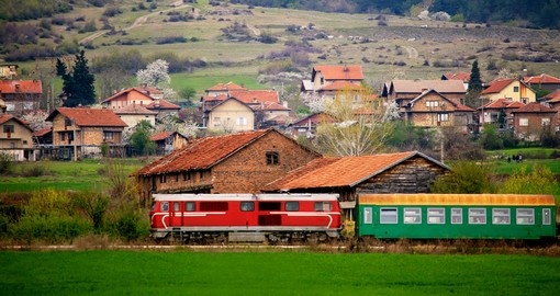 Bulgarian train passing through spring green meadows near small village