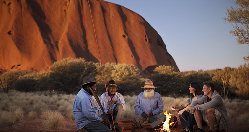 People sitting fireside before Uluru