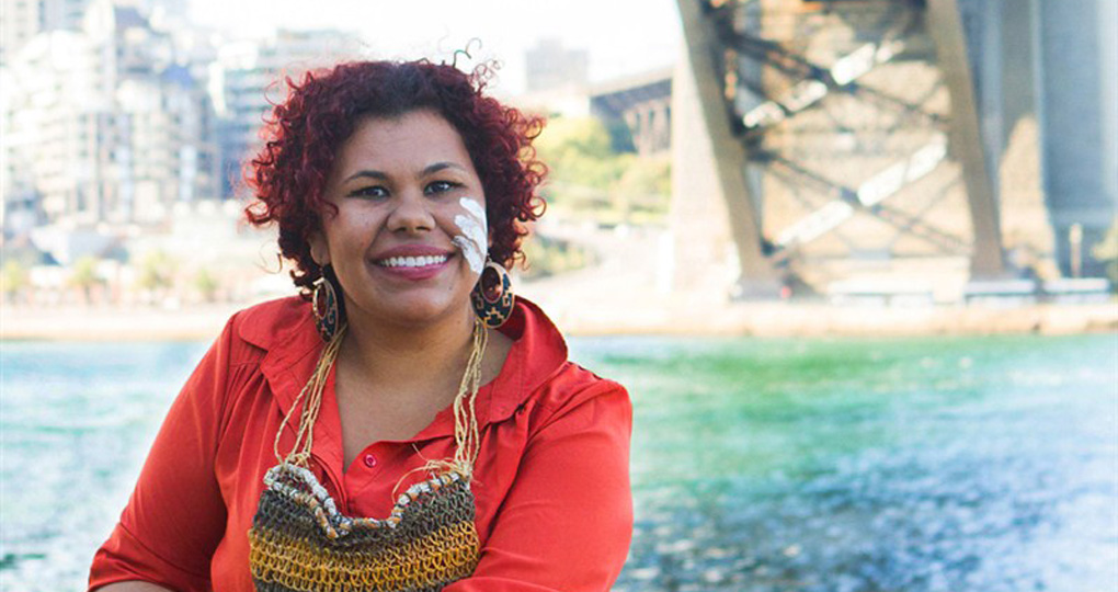 Smiling Australian Aboriginal woman in a red shirt wearing a dilly bag.