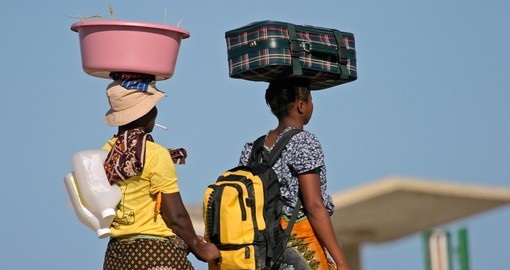 Mozambican woman in traditional dresses carrying their luggage on their heads