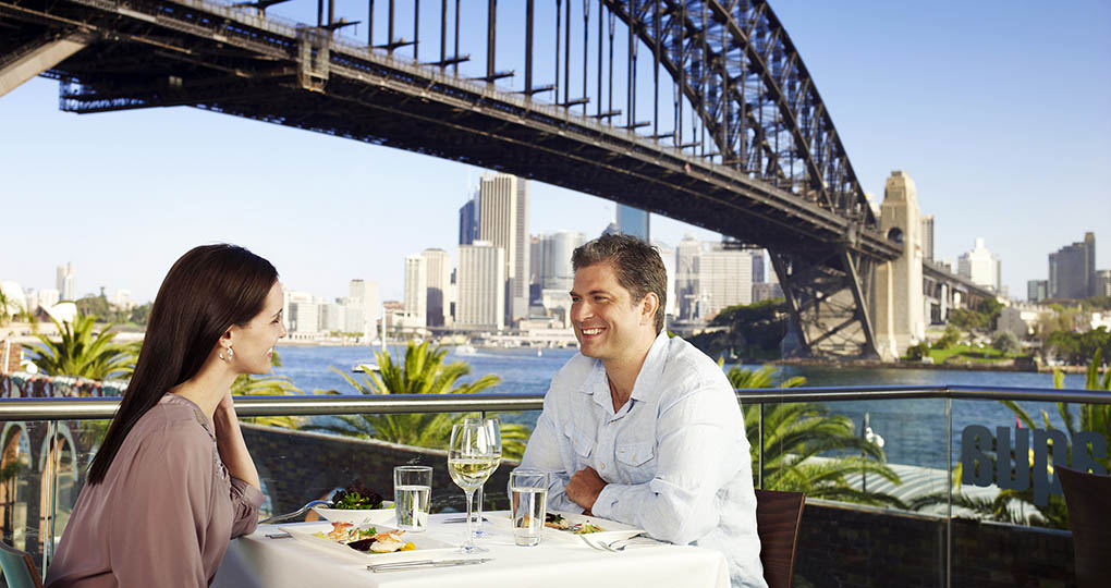 Man and woman dining outdoors in front of Sydney Harbour Bridge