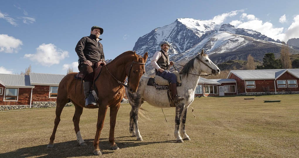 Two men riding horses with mountain in background
